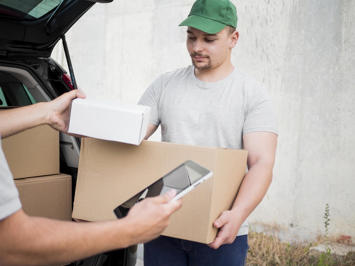 Entregador segurando caixa enquanto confere entregas com tablet. Imagem ideal para ilustrar serviços de entrega e logística.